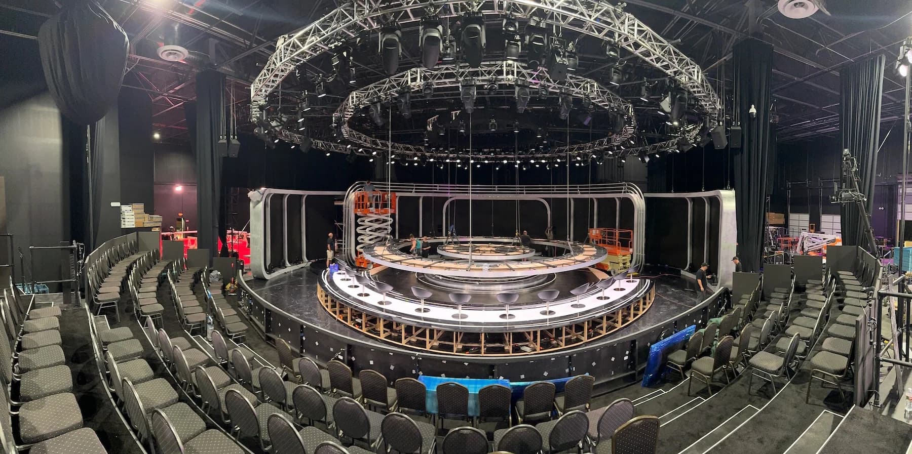 The Worre Studios stage mid-build for an in-the-round game show — a circular riser and runway ringed by tiered audience seating under a double-ring lighting truss.