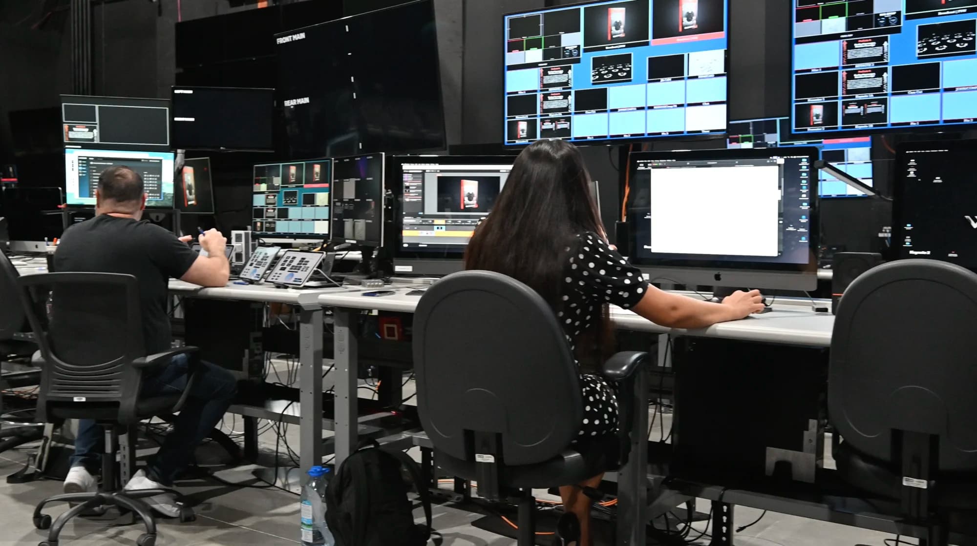 Operators running a Remote Virtual Stage broadcast from the Worre Studios control room — editors and a graphics operator at iMacs and switchers beneath multiview walls labeled Front Main and Rear Main.