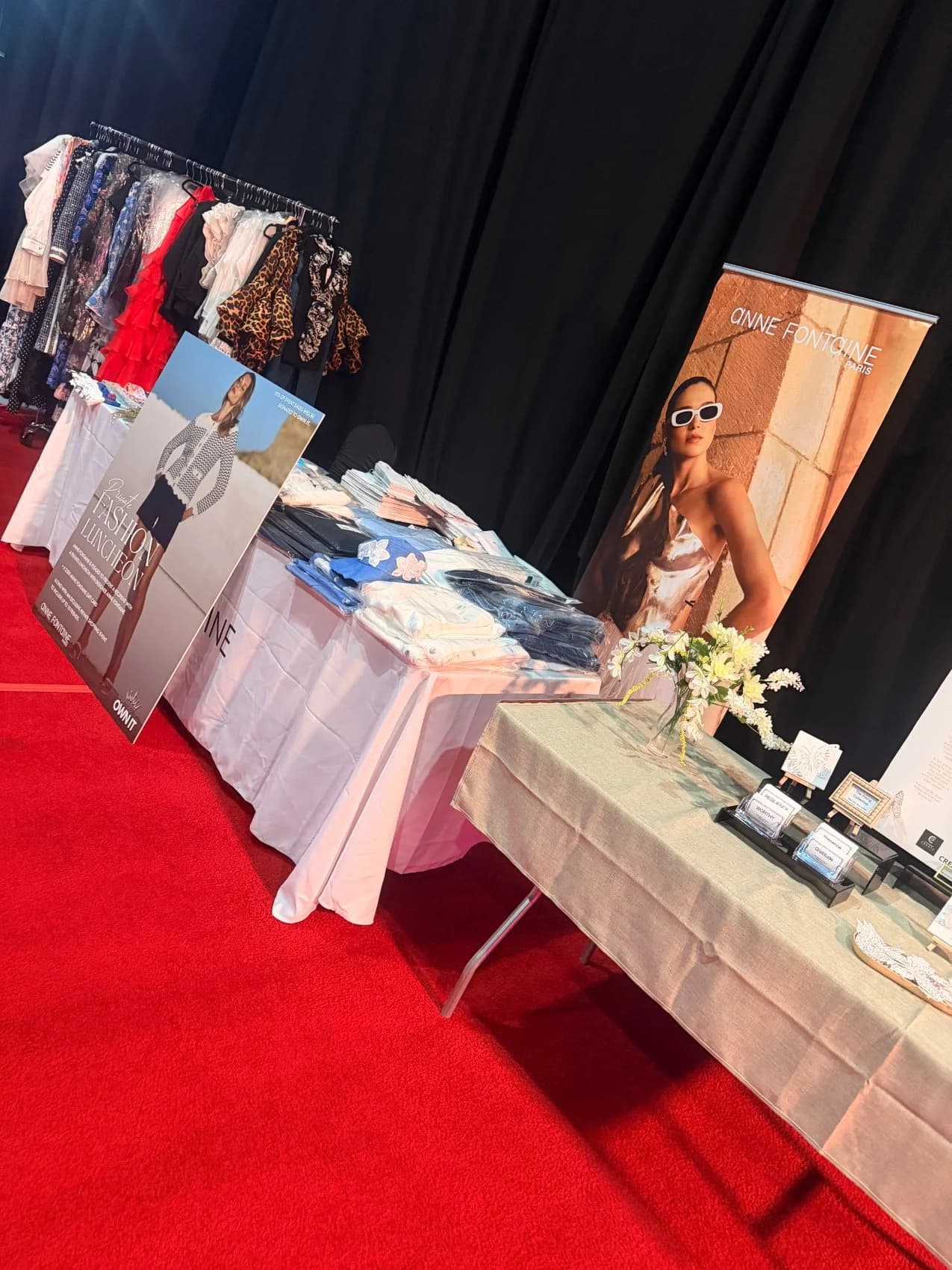 An Anne Fontaine Paris pop-up on red carpet — a clothing rack, folded apparel, and a private fashion luncheon display.
