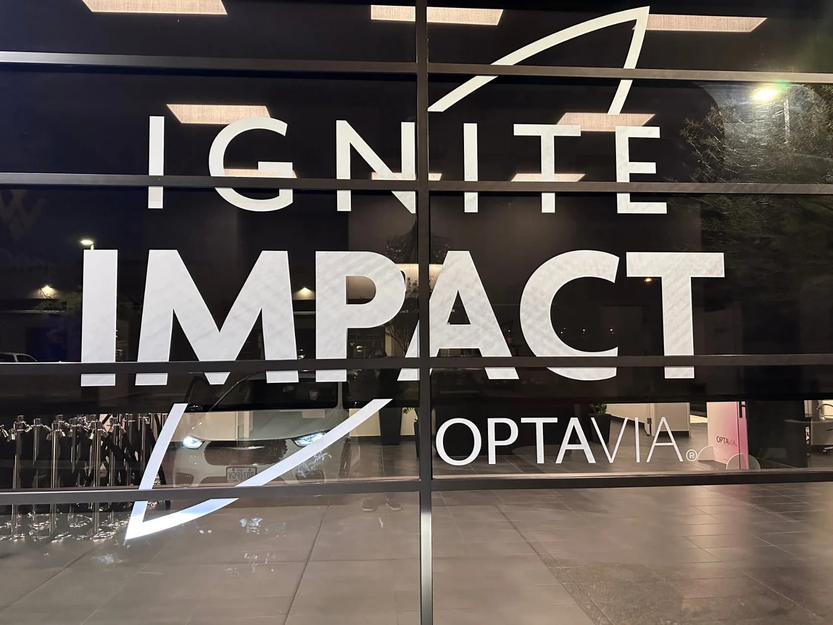 Frosted window graphics reading Ignite Impact, OPTAVIA at the studio entrance for a brand event at night.