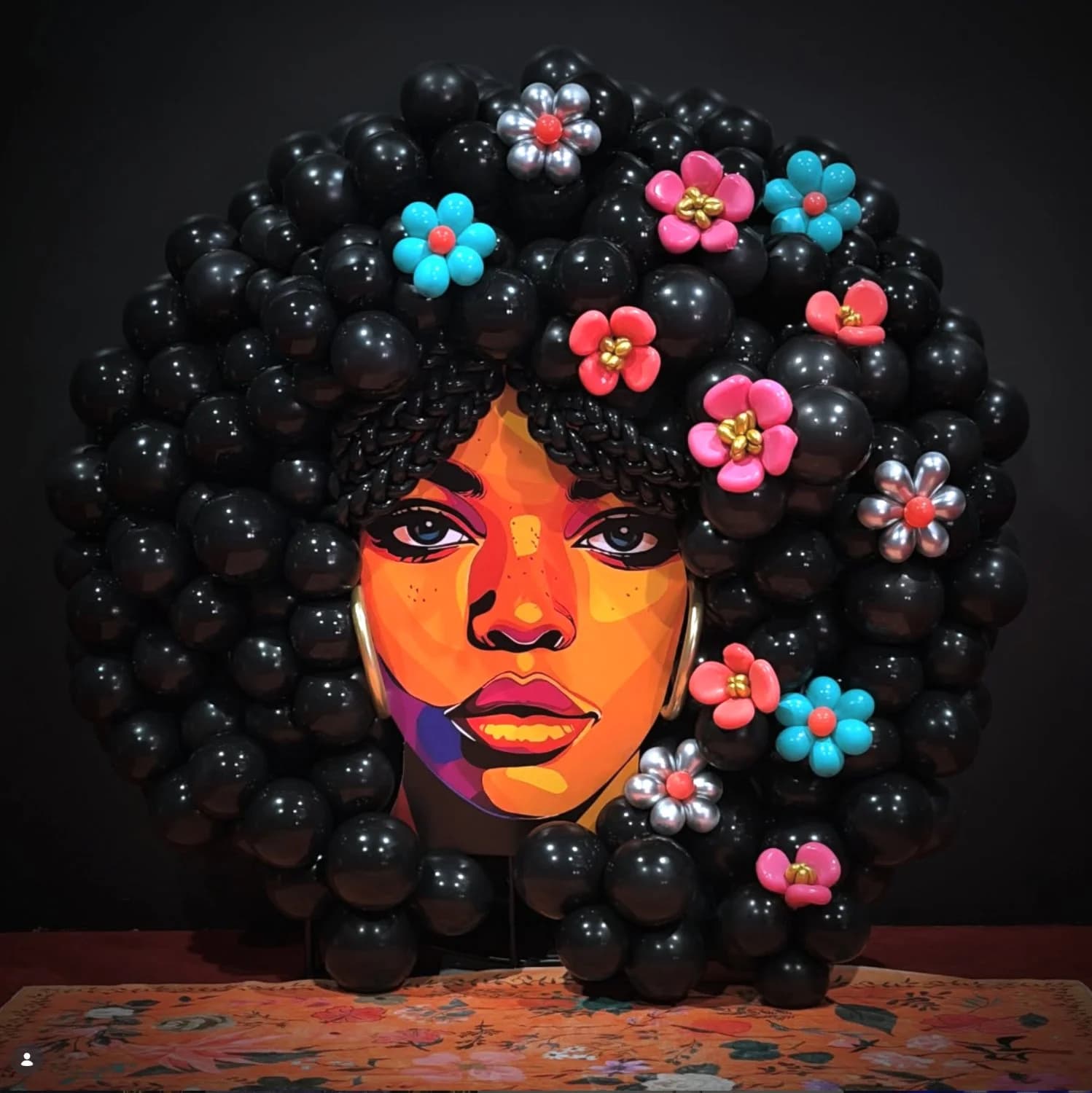 A balloon-art portrait of a woman with a flower-adorned afro built entirely from black and colored balloons for a celebration build.