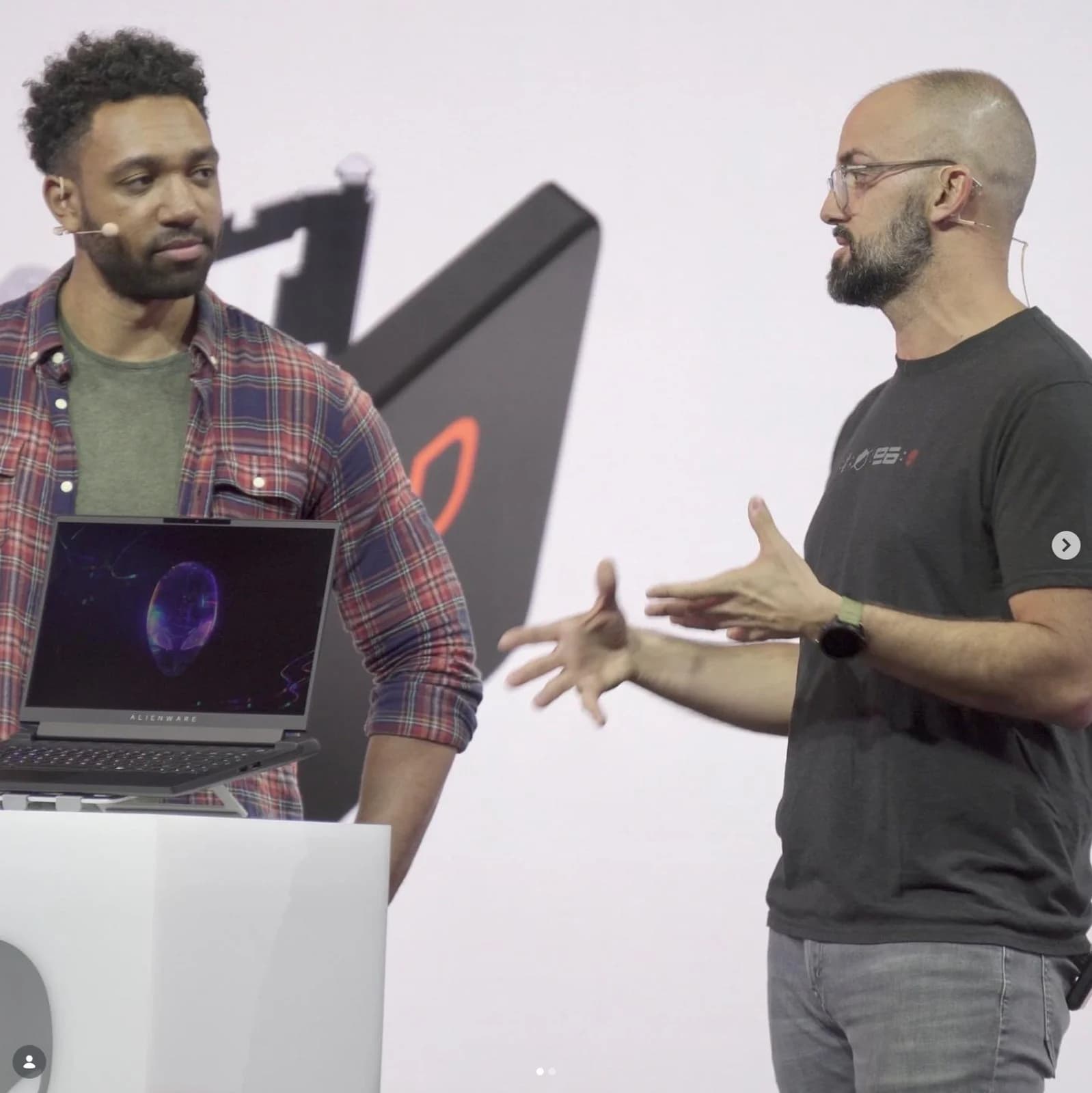 Two presenters on stage at a Dell Alienware product keynote, a gaming laptop on a plinth between them.