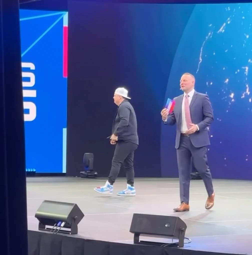 Two hosts crossing the stage in front of a blue globe graphic on the LED wall.