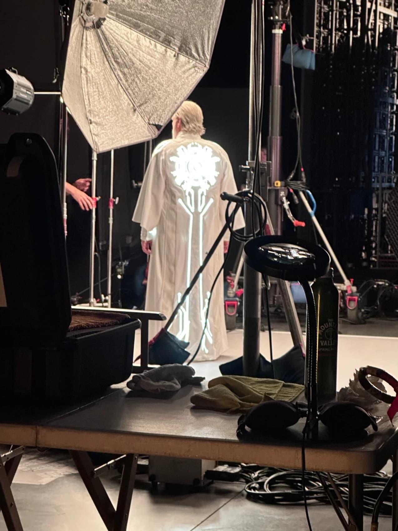 A white cyclorama and softbox lighting setup under the studio truss and crystal chandeliers, the red light-cycle visible at the rear.