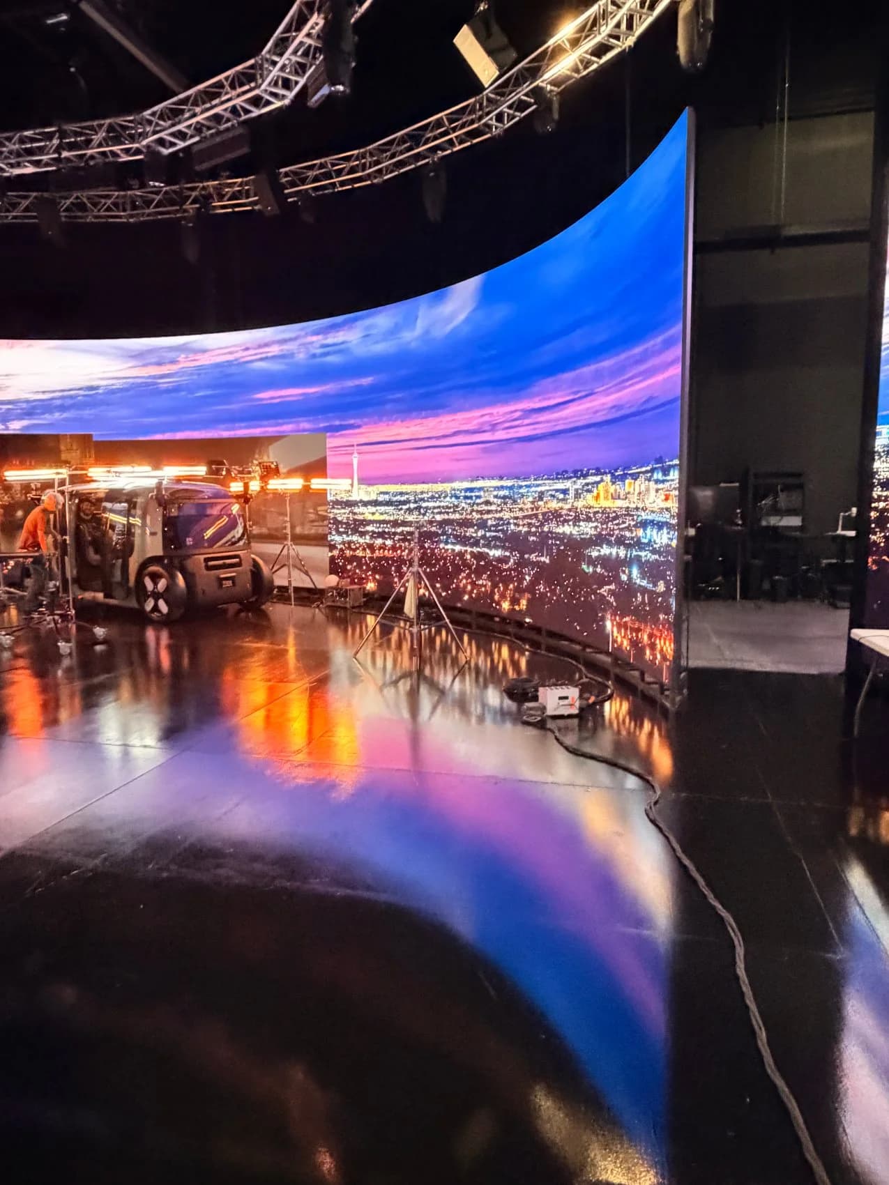 Wide view of the curved LED wall at Worre Studios rendering a Las Vegas skyline at dusk during a Zoox robotaxi shoot, crew and lights on the floor.