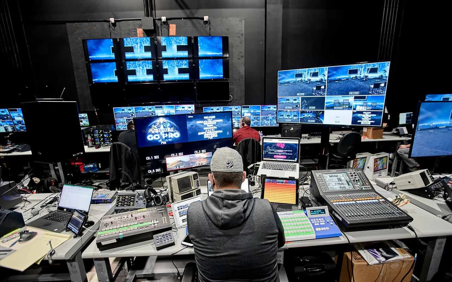 The Worre Studios broadcast control room mid-production — an engineer at a video switcher and audio console facing a wall of multiview monitors showing the live 360° LED program feeds.